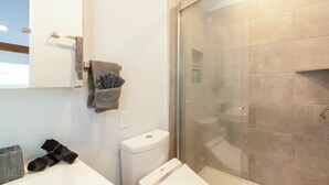 A modern bathroom with a glass-enclosed shower, a white toilet, and a towel rack with folded towels.
