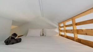 A bedroom with a wooden headboard, a neatly made bed with white linens, and a pair of shoes on the floor.