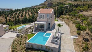 Una villa moderna con piscina, terraza cubierta y vistas a las colinas circundantes.