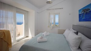Un dormitorio con cama, ventana con cortinas, un cuadro de delfines y vista al mar.