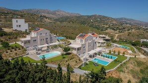 A modern residential complex with multiple buildings, swimming pools, and a mountainous backdrop.