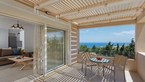 A balcony with a view of the sea, a dining table with chairs, and a sofa with cushions.