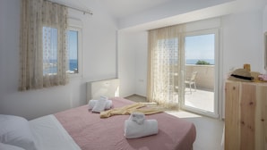 A bedroom with a bed, a wooden desk, a chair, and a view of the sea through a sliding glass door. - Blue Hills Villas by Estia, Green 3 (Ammoudi)