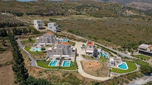 A residential complex with multiple buildings, swimming pools, and a hilly landscape in the background. - Blue Hills Villas by Estia, Green 3 (Ammoudi)
