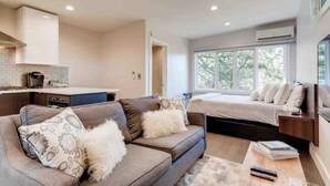 Ein modernes Wohnzimmer mit einer Couch, einem Couchtisch und einem Fernseher. Es gibt eine Küchenzeile mit einem Herd und einem Fenster.