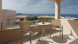 A balcony with two chairs and a table, overlooking a scenic view of the sea and distant buildings.