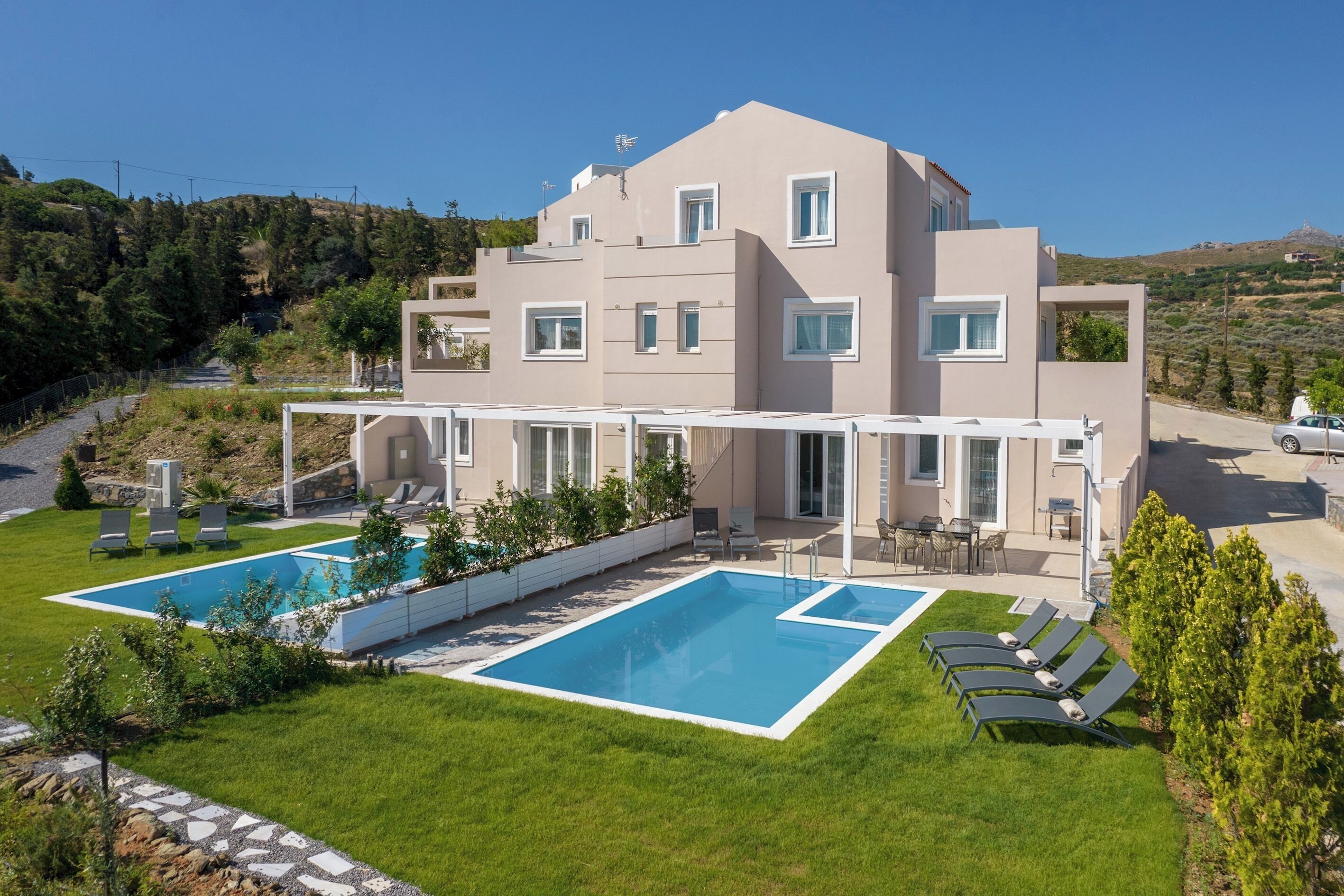 Ein modernes, zweistöckiges Haus mit Swimmingpool, Sitzgelegenheit im Freien und Blick auf die umliegenden Hügel.