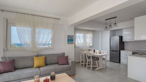 A modern living room with a grey sofa, a wooden coffee table, and a dining area with a white table and chairs.