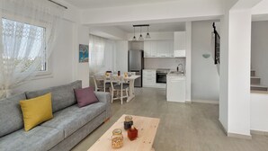 A modern living room with a grey sofa, a wooden coffee table, and a dining area with a white table and chairs.