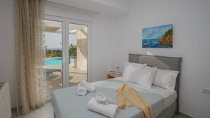 A hotel room with a bed, a painting of a coastal scene, a view of a pool, and a sliding glass door to the outdoors. - Blue Hills Villas by Estia, White 3 (Ammoudi)