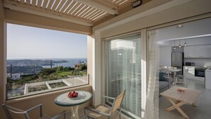 A balcony with a table and chairs, a view of the sea, and a modern kitchen visible through a glass door. - Blue Hills Villas by Estia, White 3 (Ammoudi)