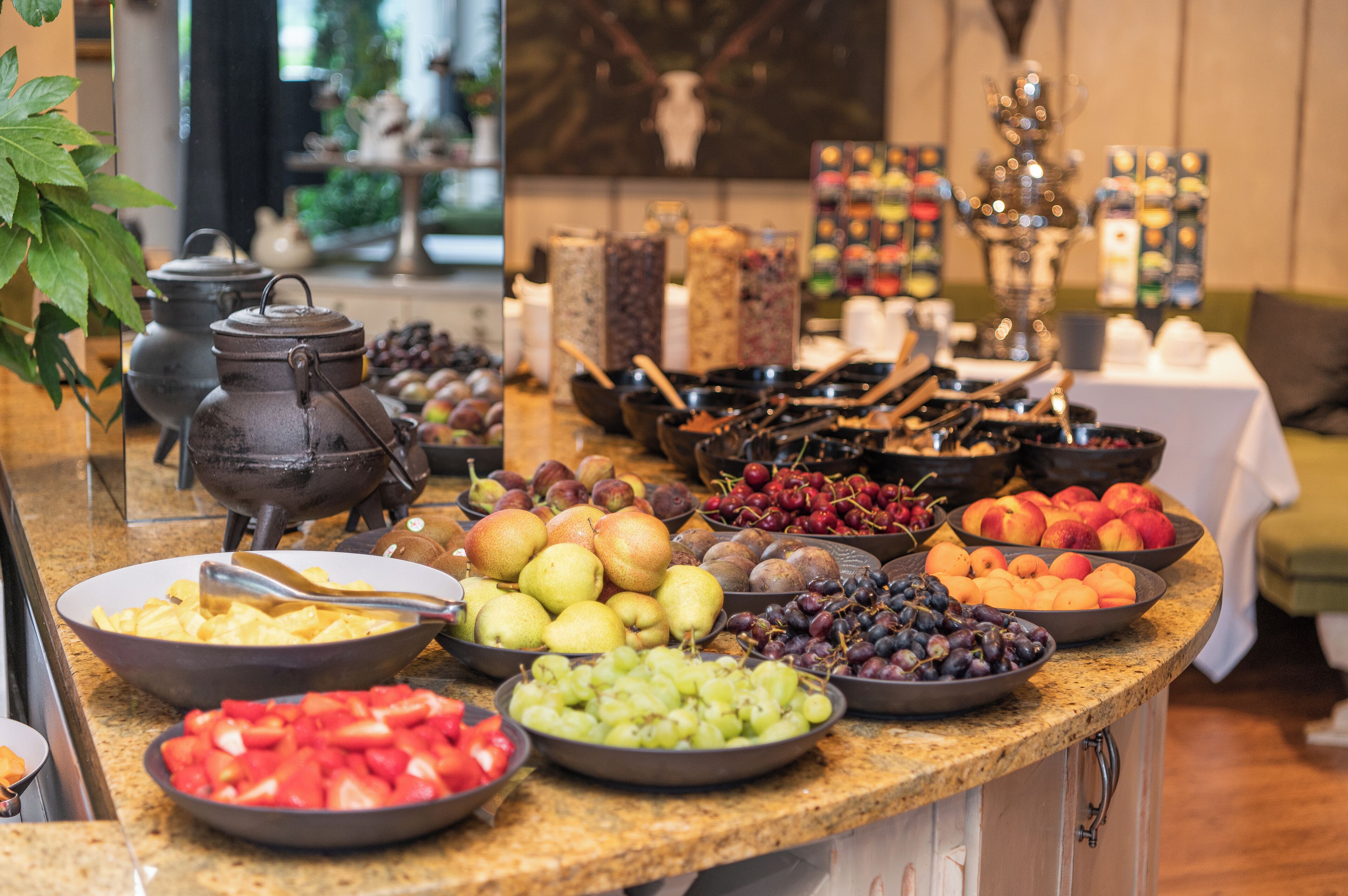 Una mesa de buffet con diversas frutas y fuentes de comida, una tetera y velas.