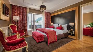A hotel room with a large bed, red and white bedding, a chandelier, and a view of a mountain.