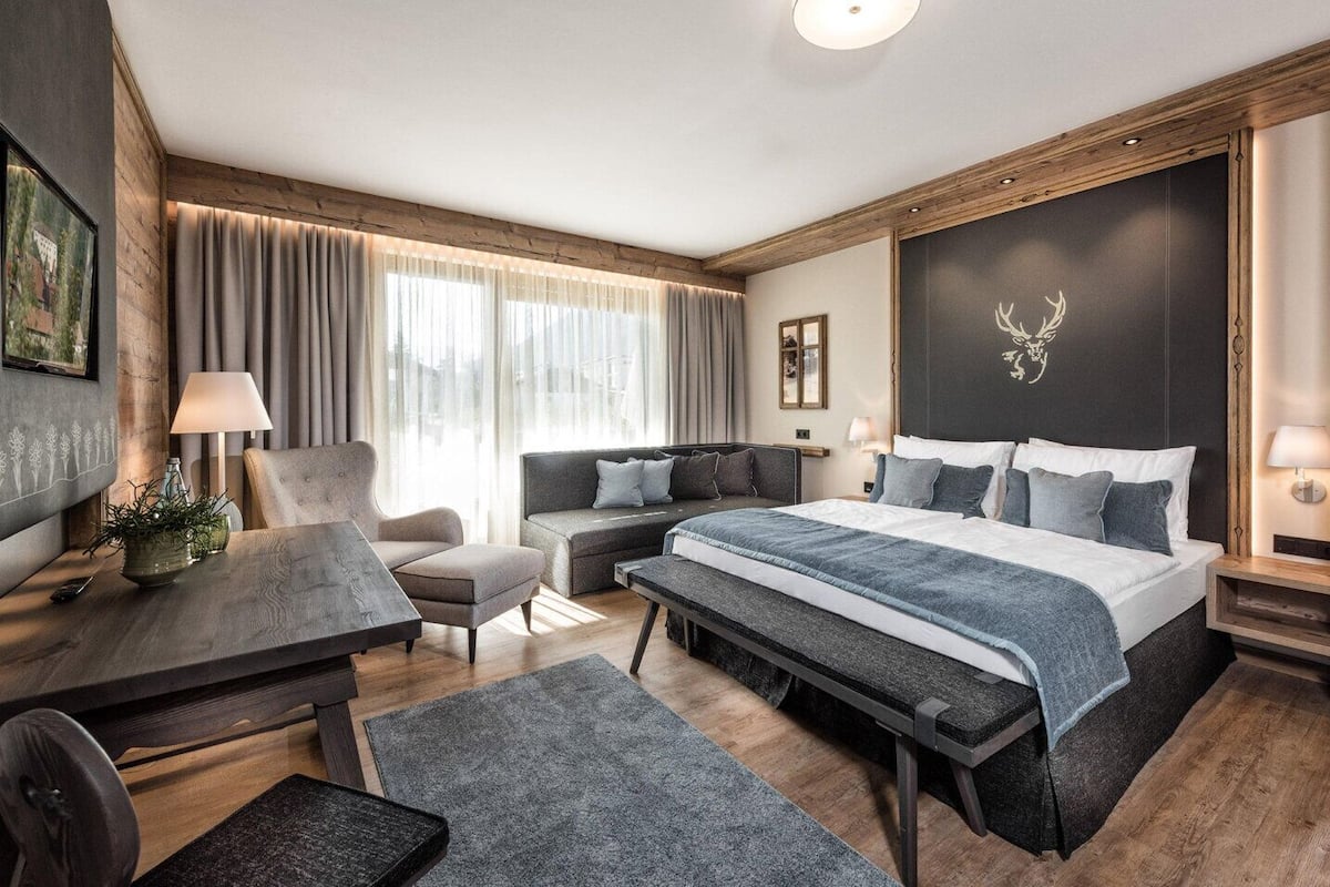 A modern hotel room with a large bed, a desk, a sofa, and a dining table.