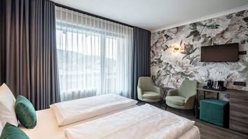 A hotel room with two beds, a desk, a chair, a TV, and a floral wallpaper.