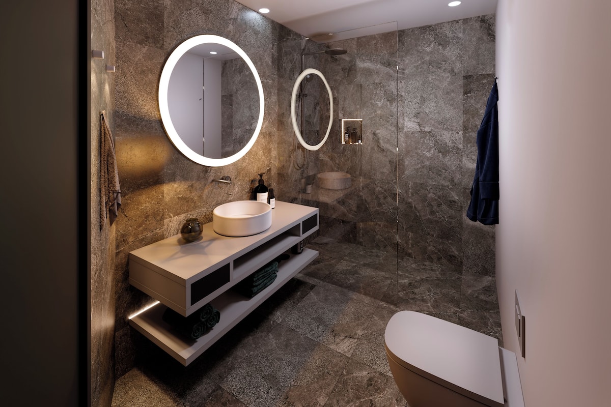 A modern bathroom with a round mirror, a sink, and a toilet.