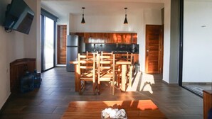 A modern kitchen with wooden cabinets, a dining table with chairs, and a flat-screen TV mounted on the wall. - Edificios Regam (El Cuyo)