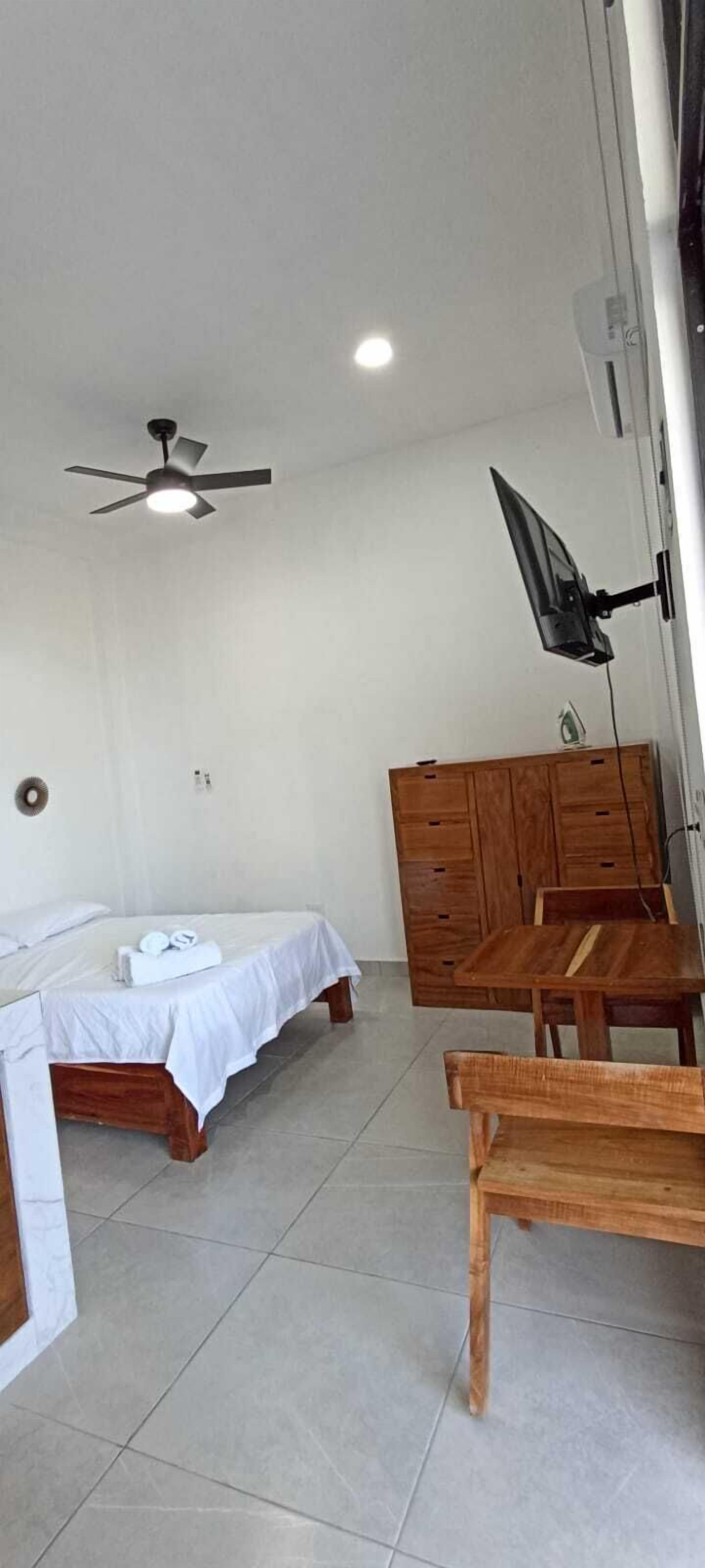 A room with two beds, a ceiling fan, a wooden wardrobe, and a table.