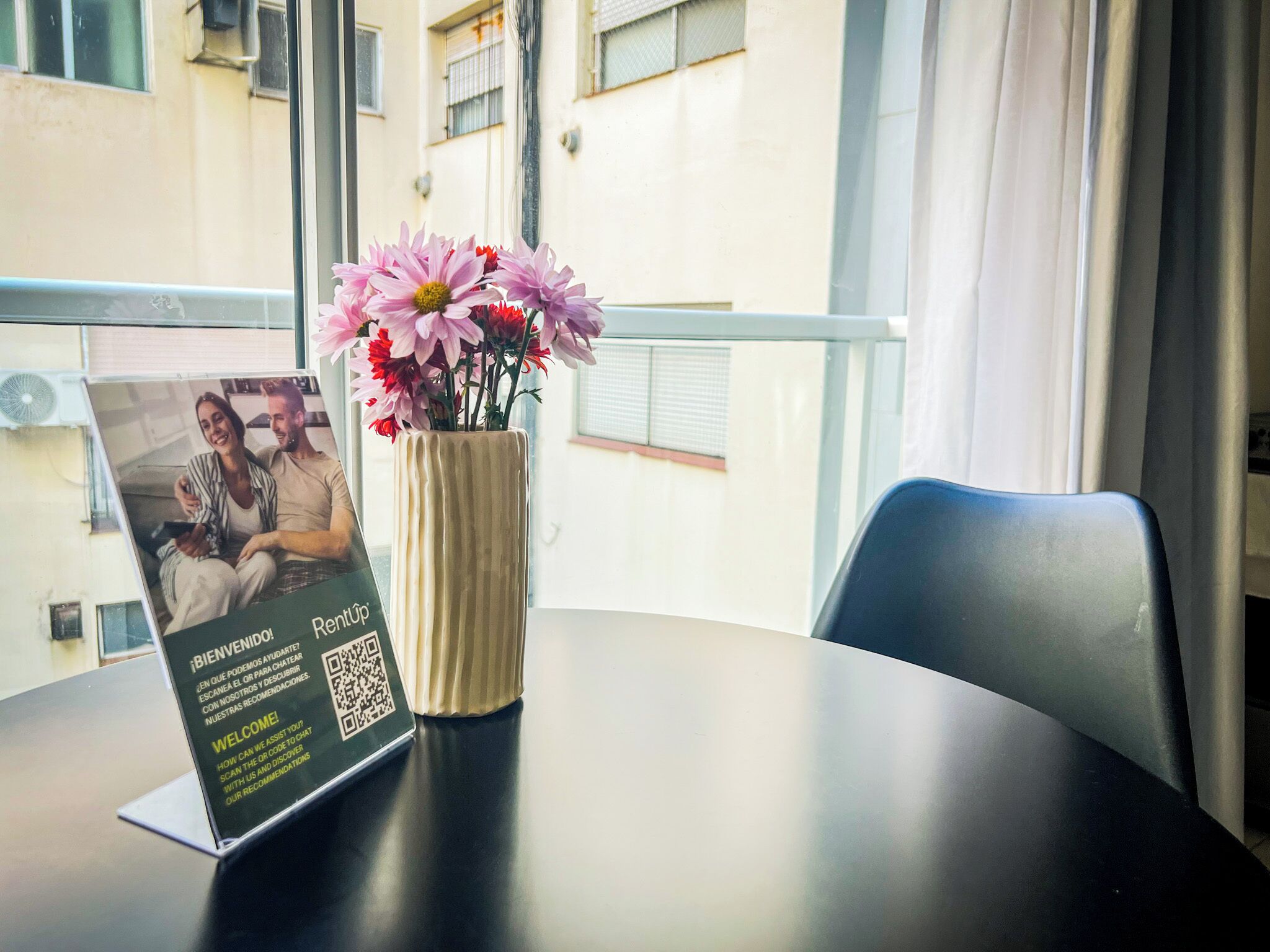 A table with a laptop displaying a welcome sign and a vase with flowers.
