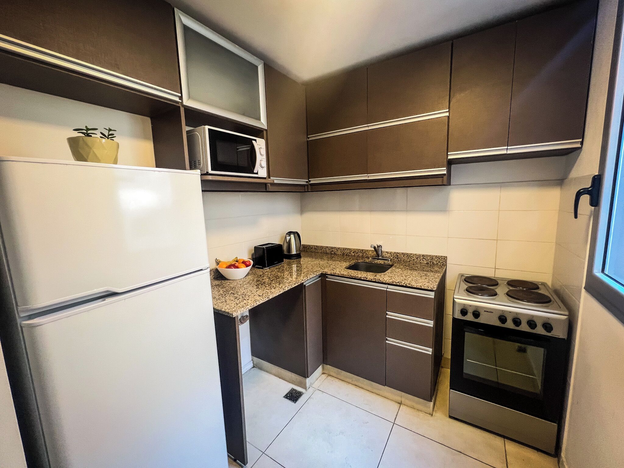 Una cocina compacta con refrigerador, microondas, tostadora, hervidor, pileta y estufa.