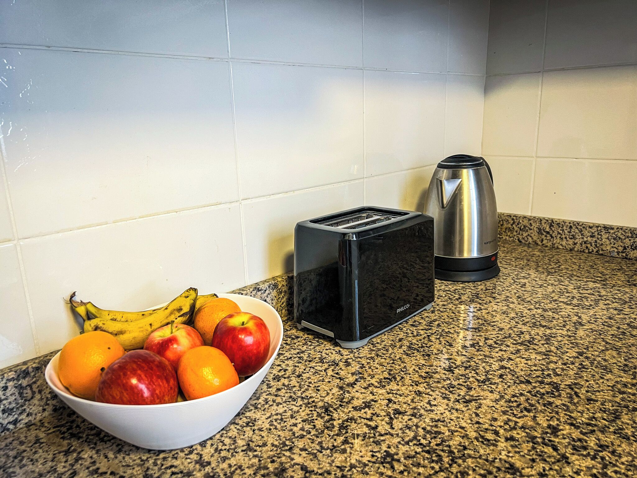A kitchen counter with a bowl of fruit, a toaster, and a coffee maker.