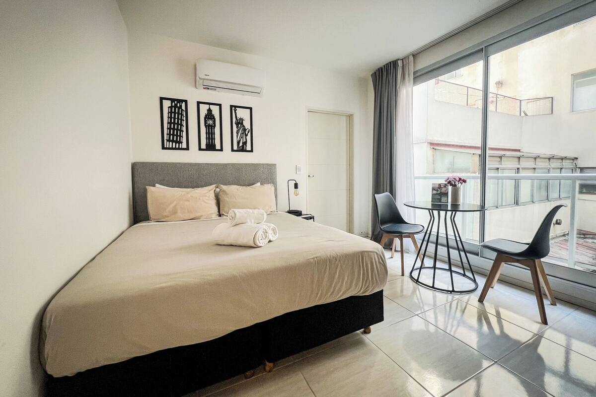 A hotel room with a bed, a small table with chairs, and a balcony with a view.