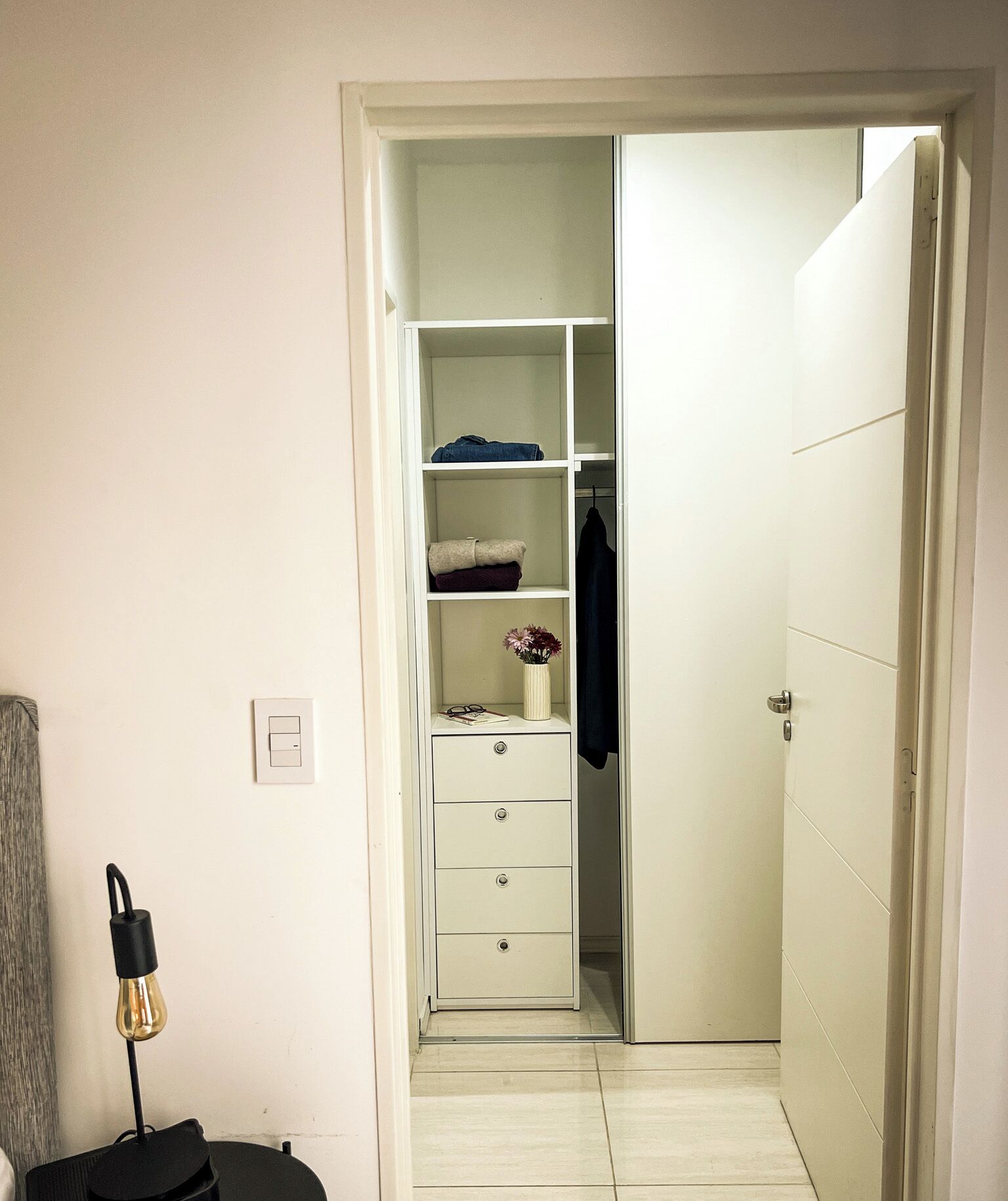 A walk-in closet with white shelving, a hanging rod, and a door with a handle.