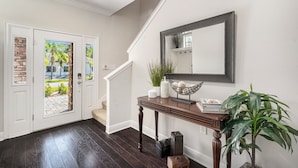 A hallway with a dark wooden floor, white doors with a brick pattern, a staircase, a console table with decorative items, and a large mirror on the wall. - Spacious 4BR pool home, billiards, BBQ, large patio, pool and pool deck (Tampa)