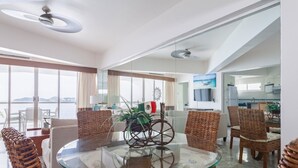 A modern living room with a glass coffee table, wicker chairs, and a view of the sea.