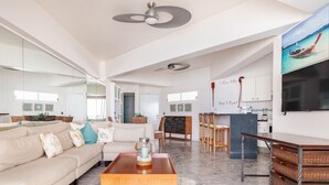 A spacious living area with a sofa, coffee table, and a dining area with chairs and a small kitchen in the background.