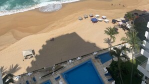 A beach resort with a pool area, beach umbrellas, and a view of the ocean.