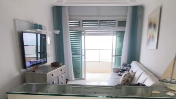 Uma sala de estar ampla, com uma ilha grande de vidro, uma TV de tela plana e um sofá.