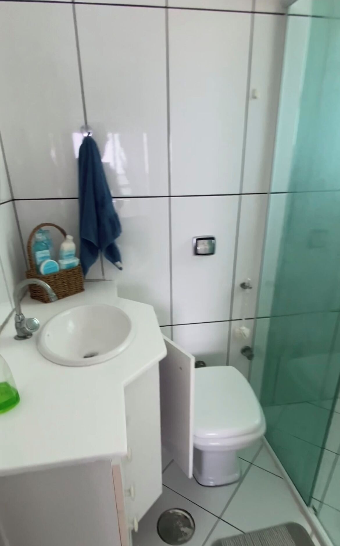 A bathroom with a white sink, a small trash bin, a toilet, and a glass shower enclosure.