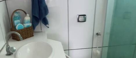 A bathroom with a white sink, a small trash bin, a toilet, and a glass shower enclosure.