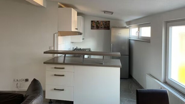 A compact kitchen with a central island, white cabinetry, and a built-in oven. - Apartment Ndé (Abstatt)