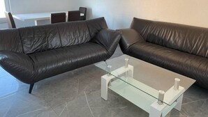 A modern living room with two leather sofas, a glass coffee table, and a dining area with chairs and a table. - Apartment Ndé (Abstatt)