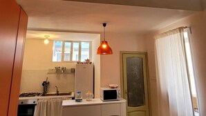 Une cuisine compacte équipée d’une cuisinière à gaz, d’un évier et d’un four à micro-ondes. Un luminaire est suspendu au-dessus du plan de travail.