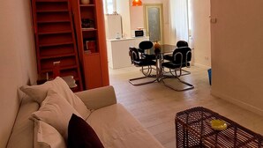 Un salon avec un canapé, une table à manger avec des chaises, un coin cuisine et un escalier.