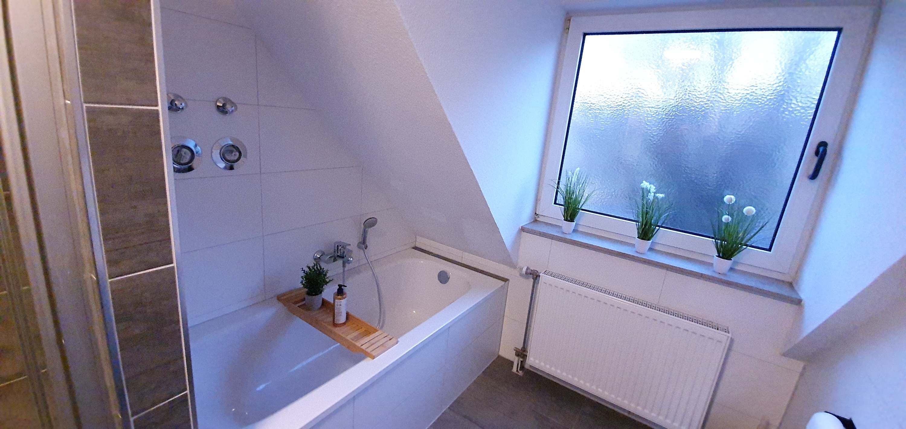 A bathroom with a bathtub, a shower, a window with plants, and a radiator.