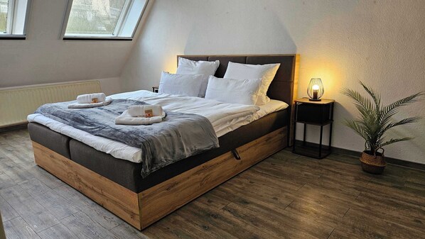 A modern bedroom with a wooden bed frame, white bedding, a bedside lamp, and a potted plant. - Wohlfühlapartment - 3 Schlafzimmer - Dachterrasse (Eisenach)