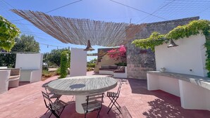 Um pátio com mesa e cadeiras redondas, uma pérgola e uma parede de pedra coberta de vegetação.