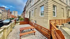 A courtyard with wooden benches and a picnic table, surrounded by a low stone wall. - City Haven Main Door & Parking - Pass the Keys (Glasgow)