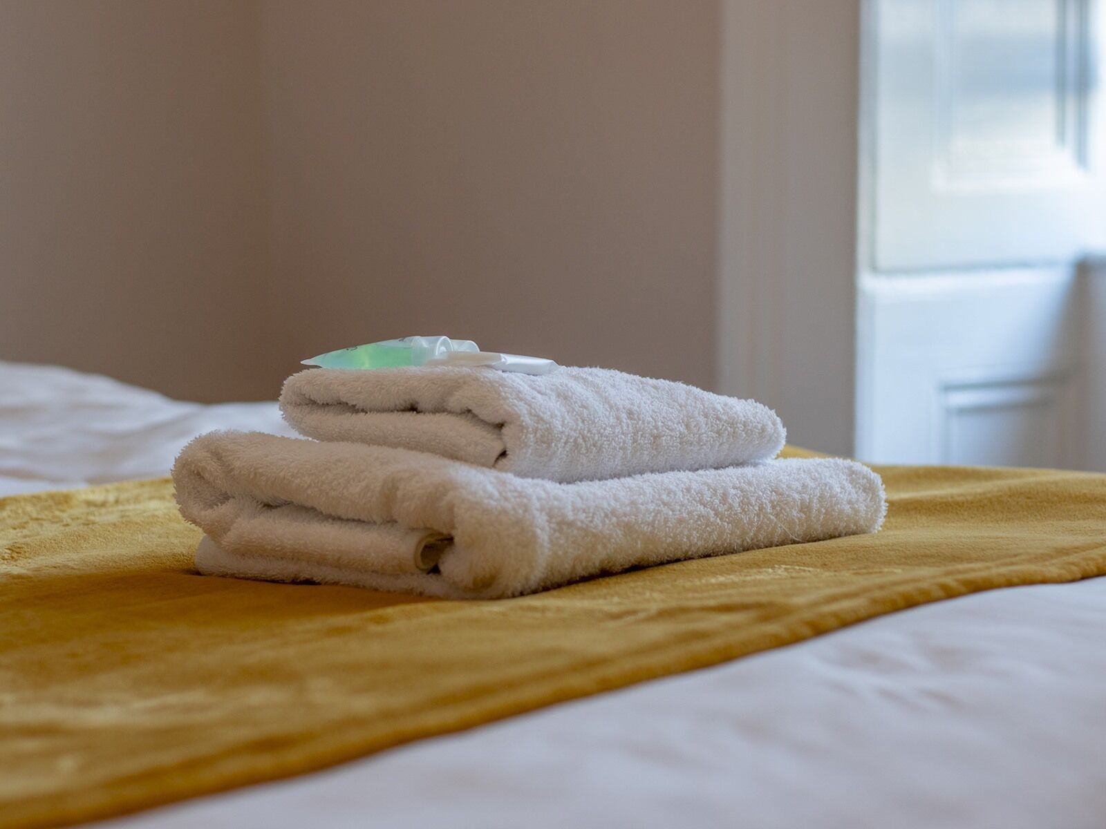 A neatly folded white towel on a yellow blanket on a bed.