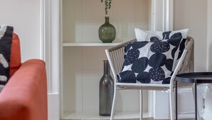 A room with a white chair with a black and white patterned cushion, a small table, and a shelf with decorative items including a green vase and a potted plant. - City Haven Main Door & Parking - Pass the Keys (Glasgow)