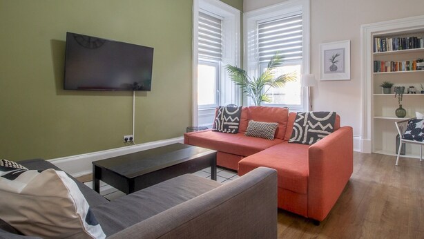 A living room with a sofa, a coffee table, a flat-screen TV, and a bookshelf. - City Haven Main Door & Parking - Pass the Keys (Glasgow)
