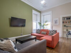 A living room with a sofa, a coffee table, a flat-screen TV, and a bookshelf. - City Haven Main Door & Parking - Pass the Keys (Glasgow)