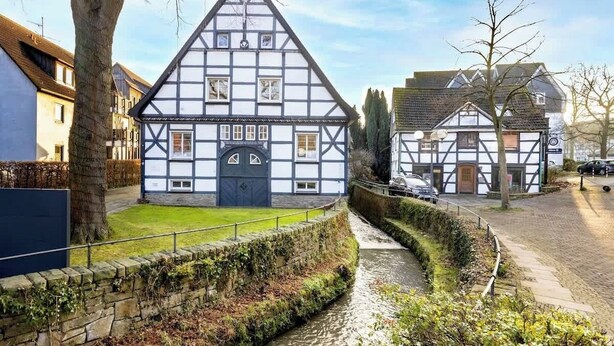 A traditional half-timbered house with a stone wall and a narrow water channel in front. - MOLA Apartments-Historisches Apartment in Altstadt (Herdecke)