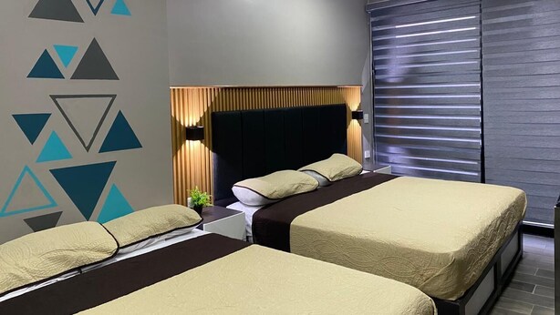 A modern hotel room with two beds, a large window with blinds, a geometric wall design, and a headboard with integrated lighting. - Hotel Felix (San Juan de los Lagos)
