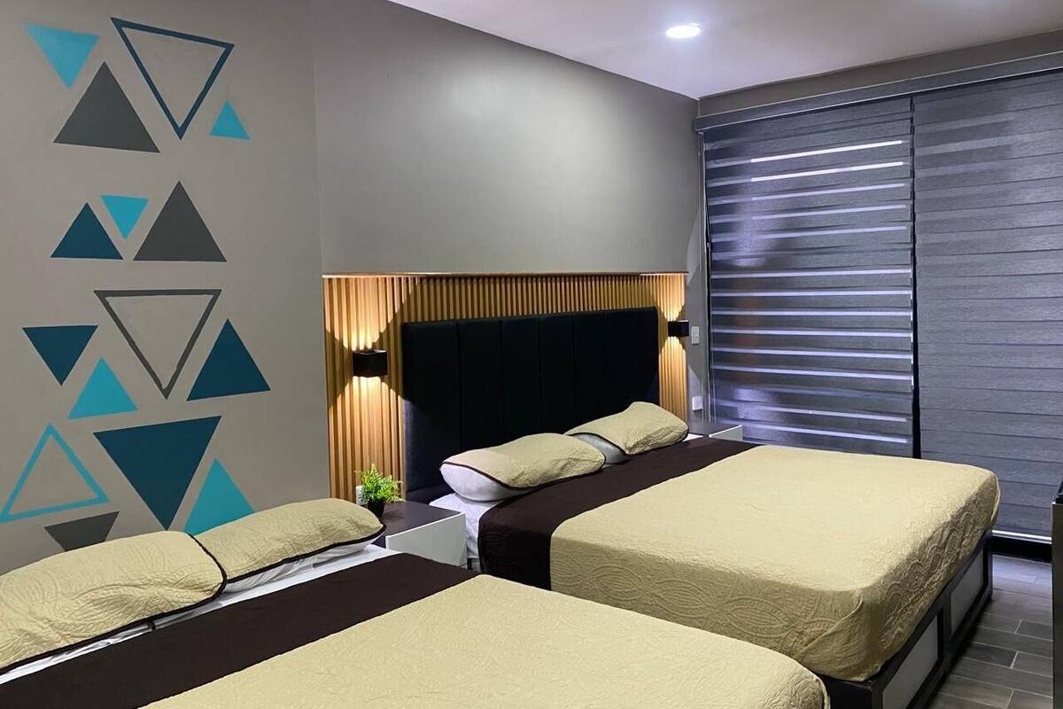 Een moderne hotelkamer met twee bedden, een groot raam met zonwering, een geometrisch wandontwerp en een hoofdeinde met ingebouwde verlichting.