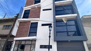 A multi-story building with a modern architectural design, featuring a mix of brick and white facades, large windows, and a visible ground-floor entrance with a glass door. - Hotel Felix (San Juan de los Lagos)